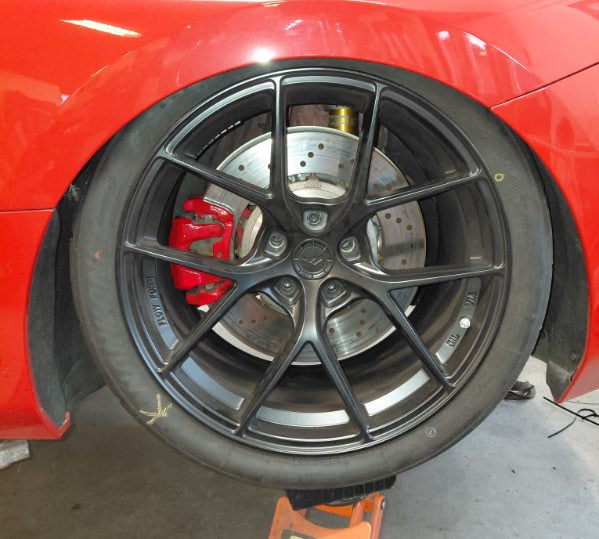 Close-up of a red car with a black alloy wheel on a lift in a garage.