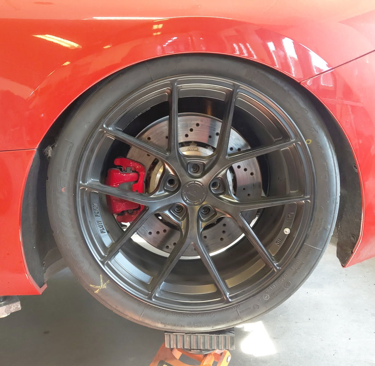 Close-up of a red car's wheel with a black rim and red brake caliper.